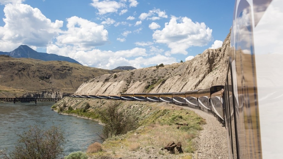 Rocky Mountaineer alongside a river with scenery and hills in the background