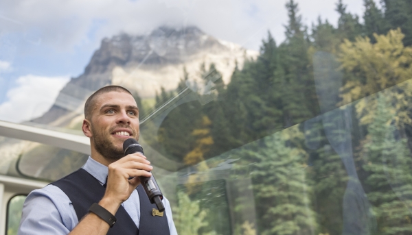 Host tells story about surrounding scenery on mic, part of Rocky Mountaineer's luxury service onboard the train.