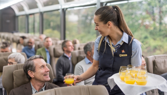 rocky mountaineer host hands out orange juice onboard the train in gold leaf service