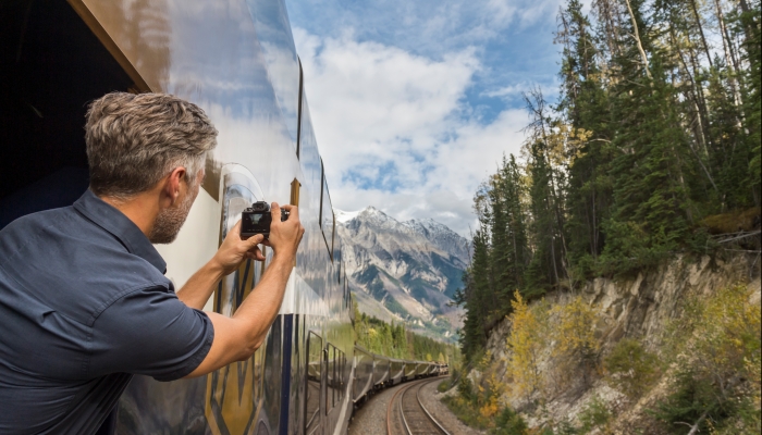 man snaps a photo of mountain range while leaning out of outdoor viewing platform on the journey through the clouds route on the way to Jasper