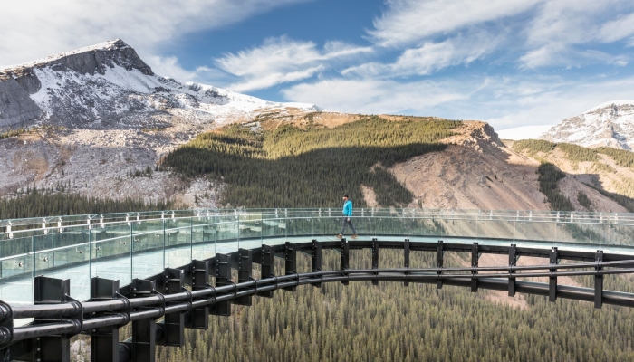 A man walking on a clear bridge with mountains in the background