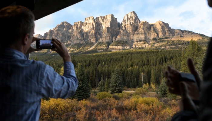 guest takes picture of Castle Mountain while onboard Rocky Mountaineer train in GoldLeaf Service