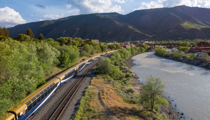 Rocky Mountaineer train travelling alongside a river on the Rockies to the Red Rocks route