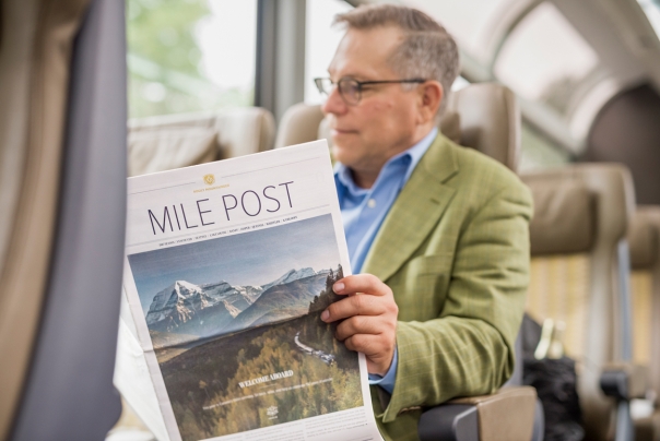 man reading mile post newspaper seated on the train