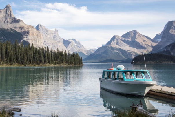 A blue and white boat rests by a dock in a lake with mountains in the background