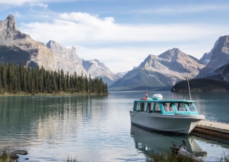 A blue and white boat rests by a dock in a lake with mountains in the background