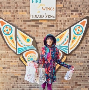 A woman in a colourful coat standing in front of butterfly wings art.