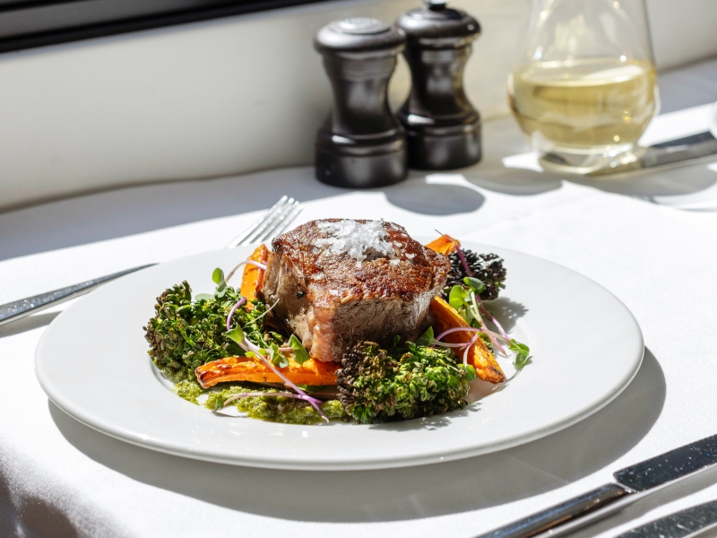 A photo of steak and vegetables on a white tableclothed table