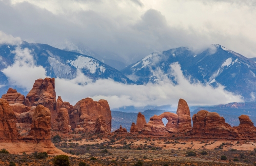 Juxtaposition of snowcapped mountains behind red rock formations in Moab.